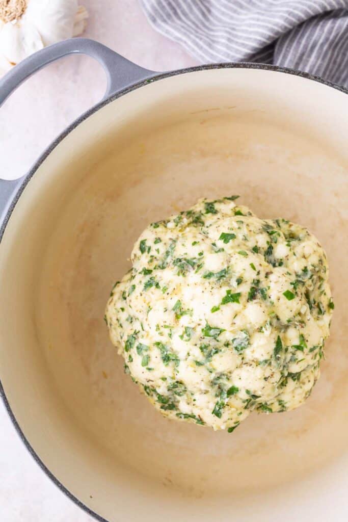 A ball of uncooked dough mixed with chopped herbs sits in the center of a large, empty pot.