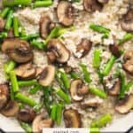 A pan of creamy risotto topped with sliced mushrooms and chopped asparagus.