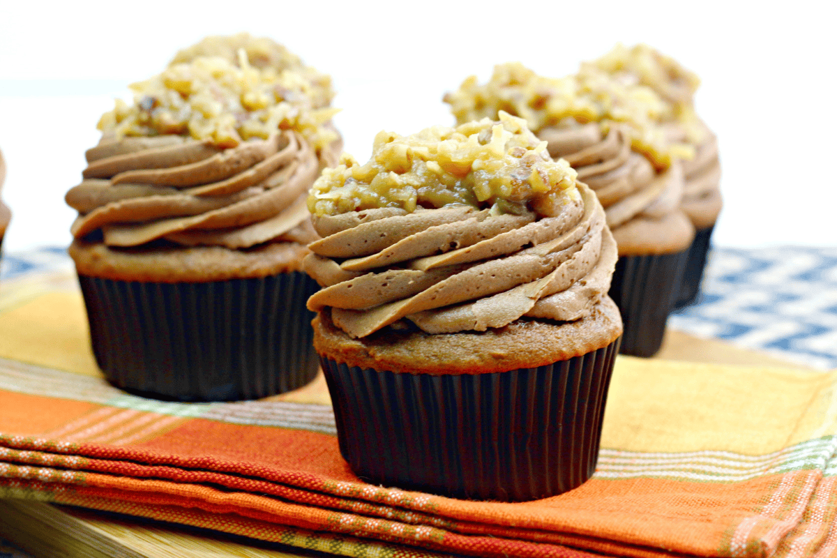 Chocolate cupcakes topped with swirled chocolate frosting and a chopped nut mixture, displayed on a stack of folded, colorful napkins.