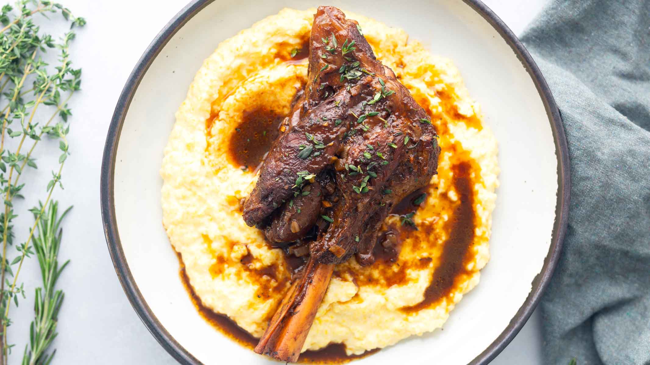 A bowl of polenta with a braised lamb shank nestled on top.