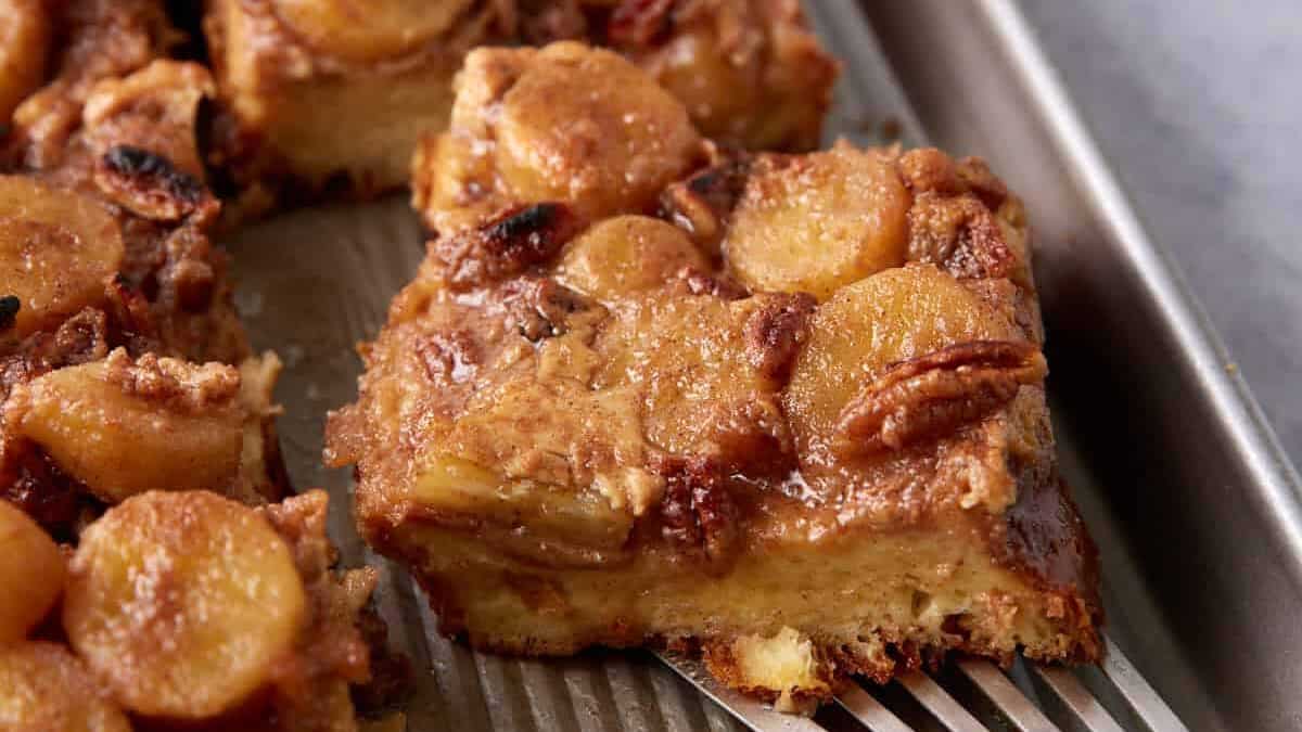 Close-up of a slice of caramelized banana and pecan bread pudding on a baking sheet, with more slices in the background.