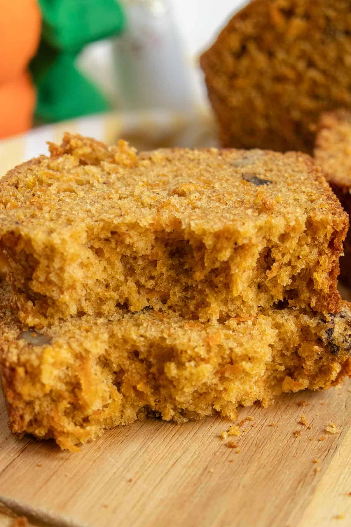 Two slices of pumpkin bread with a crumbly texture are stacked on a wooden surface.