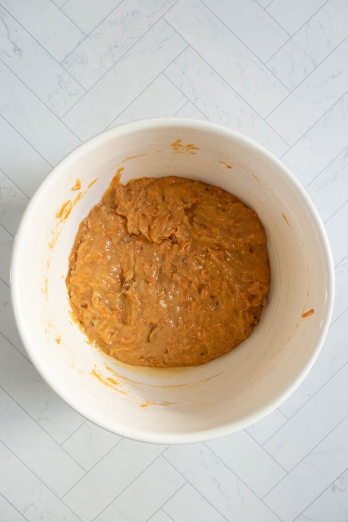 A white bowl containing thick, orange-brown batter sits on a light, tiled surface.