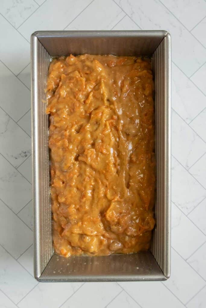 Unbaked banana bread batter in a rectangular metal loaf pan on a white tiled surface.