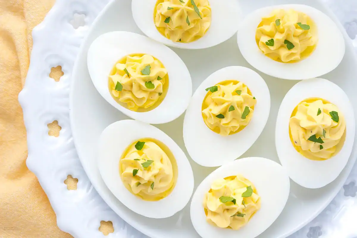 A white plate with seven deviled eggs, each topped with chopped fresh herbs, arranged neatly on a decorative dish.