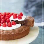 A slice of chocolate kladdkaka cake topped with whipped cream and raspberries is being served from a marble platter.