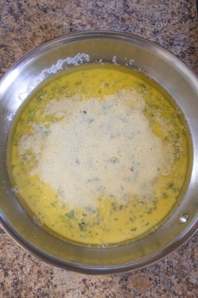 A metal pan with a yellow egg mixture, possibly for an omelet or frittata, sits on a brown marbled countertop.