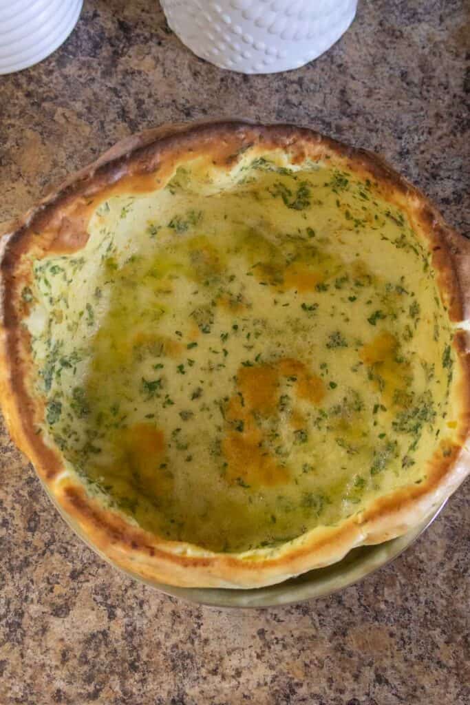 A baked spinach quiche with a puffed, golden-brown crust and a yellow-green filling sits on a brown countertop.