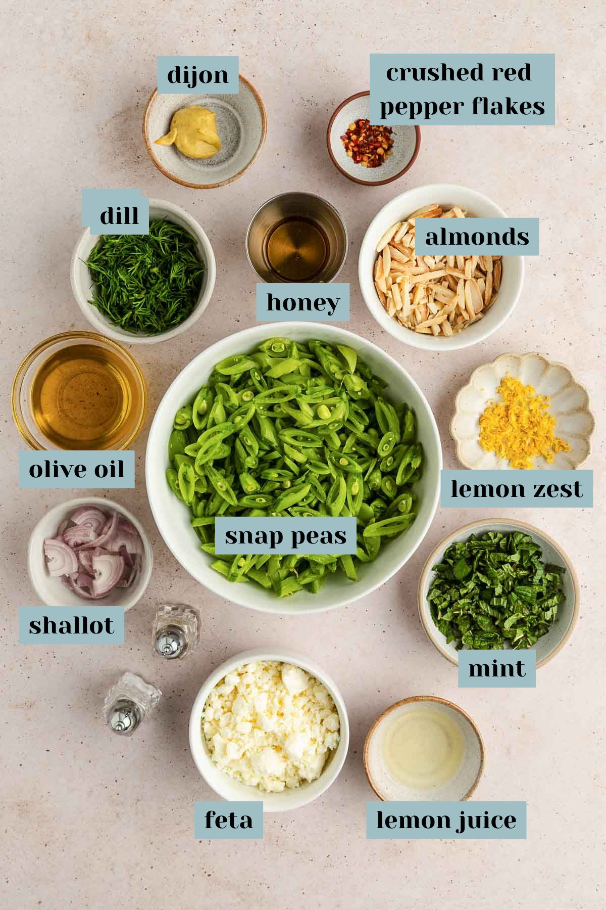 Various labeled ingredients in separate bowls, including snap peas, feta, mint, almonds, dill, shallot, honey, dijon, red pepper flakes, olive oil, lemon juice, and lemon zest.