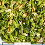 A bowl of fresh snap pea salad with sliced snap peas, red onions, herbs, crumbled cheese, and slivered almonds.