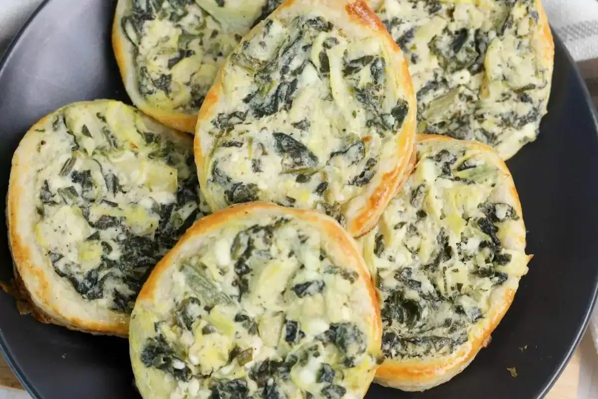 A plate of round puff pastry pinwheels filled with a creamy spinach and artichoke mixture.