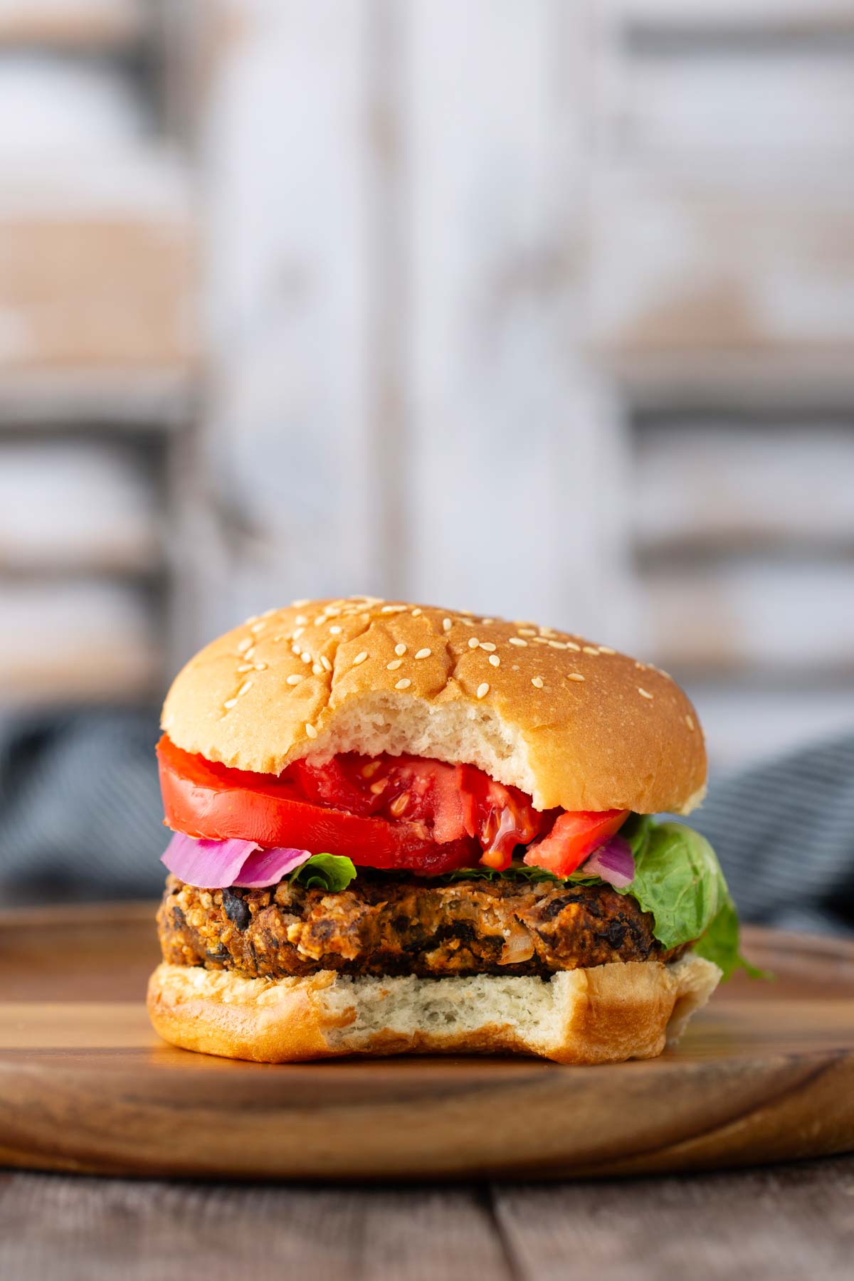 A veggie burger with lettuce, tomato, and red onion on a sesame bun, placed on a wooden surface.