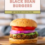 A black bean burger with lettuce, tomato, and red onion on a wooden plate; text above reads "Black Bean Burgers – Get the recipe at stetted.com.