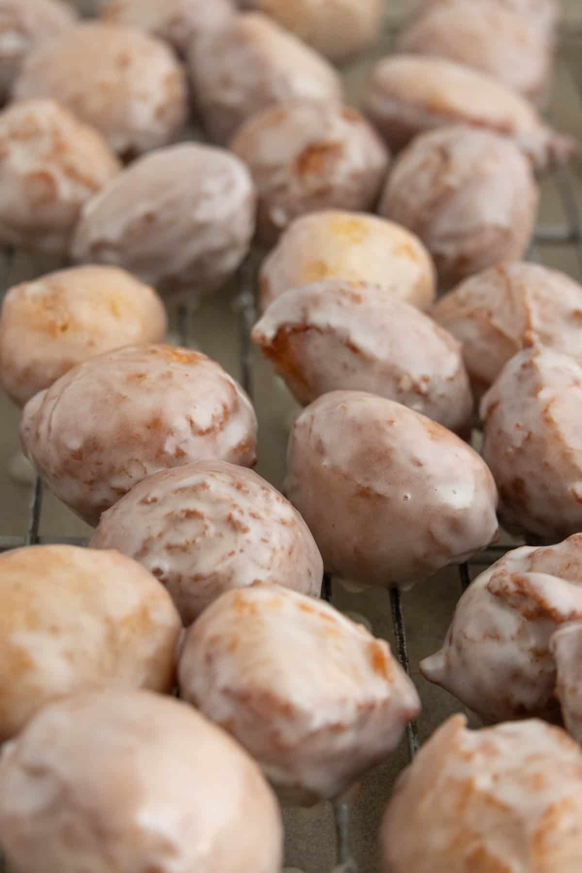 A close-up of several glazed donut holes cooling on a wire rack.
