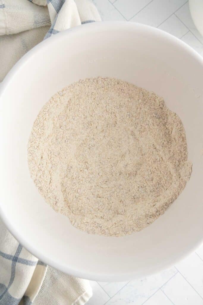 A white bowl filled with a mixture of dry flour on a light surface, with a folded towel nearby.