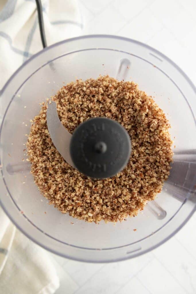 Chopped nuts in a food processor, viewed from above, with the blade visible in the center of the container.