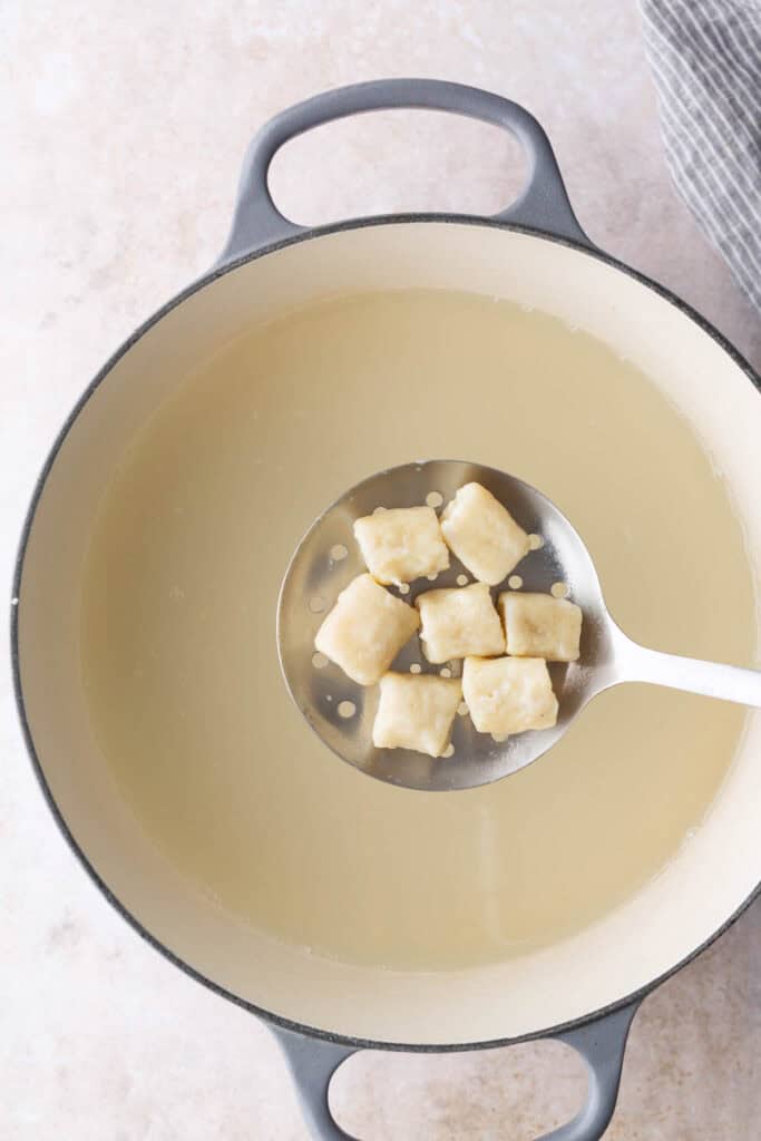 A slotted spoon holds several cooked gnocchi pieces above a pot of hot water.