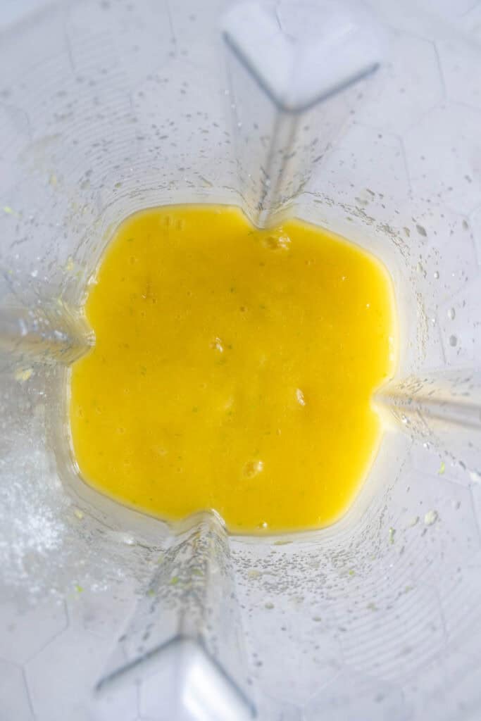 Yellow liquid mixture at the bottom of a blender viewed from above, with some splatters on the blender sides.
