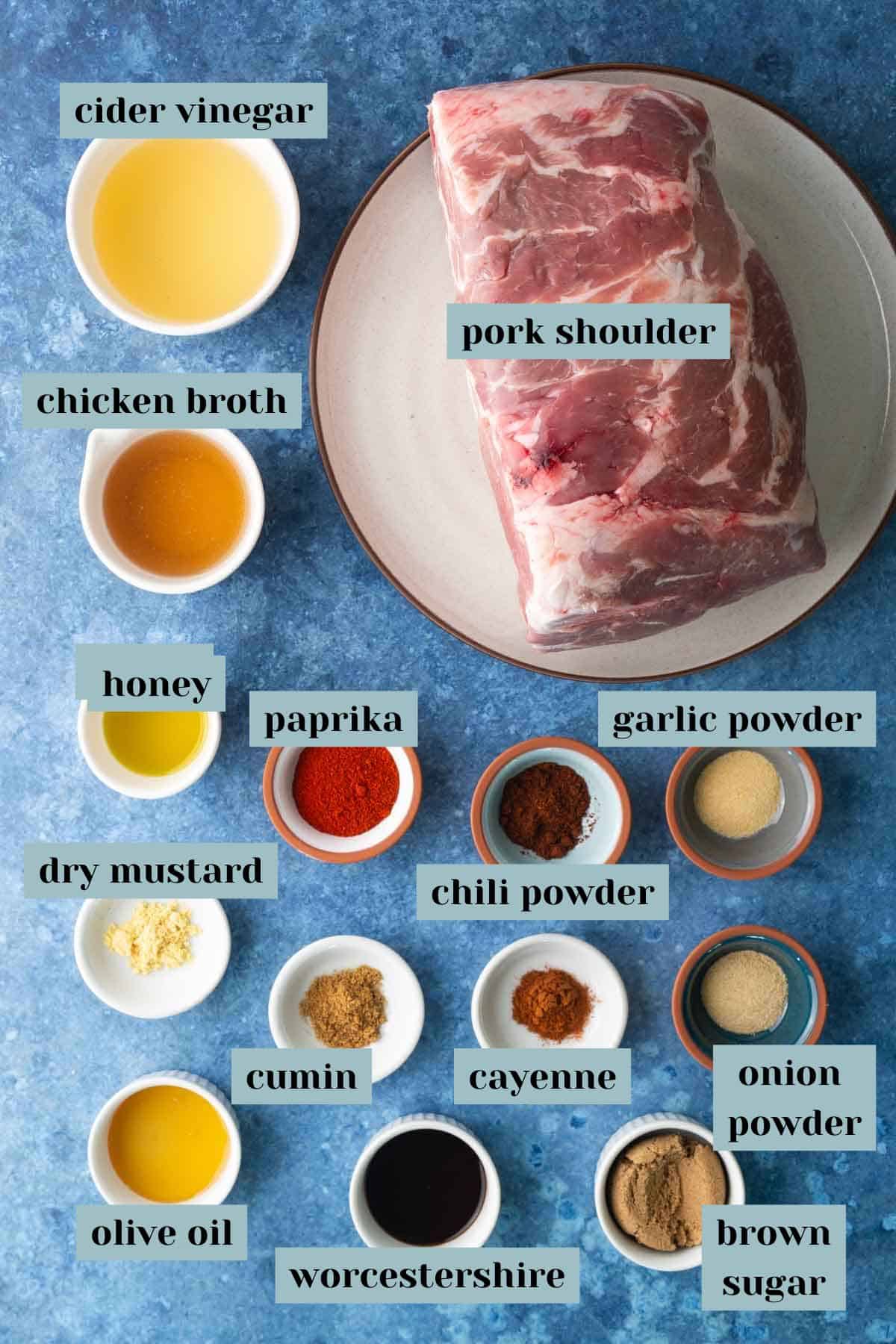 A raw pork shoulder on a plate surrounded by bowls of cider vinegar, chicken broth, honey, olive oil, Worcestershire, spices, brown sugar, and seasonings on a blue surface.