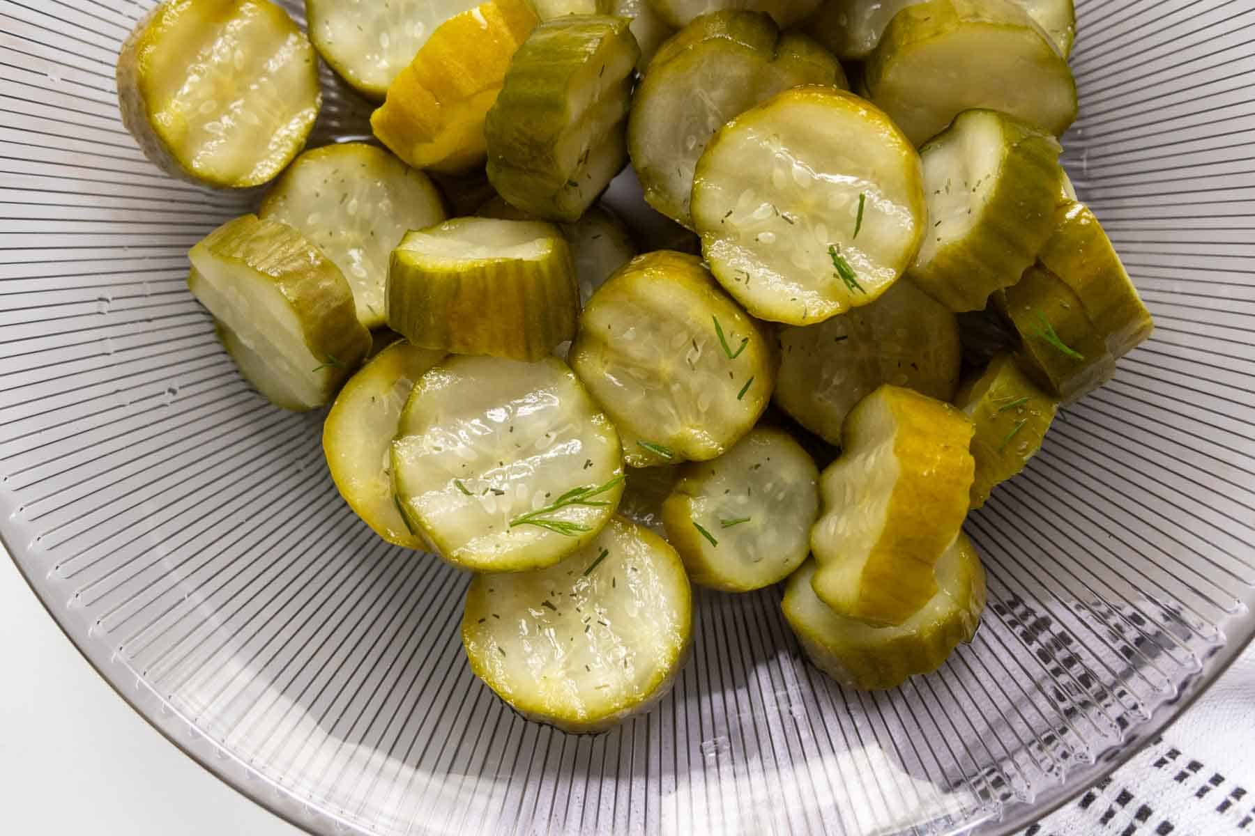 Sliced pickles with dill on a white plate, viewed from above.