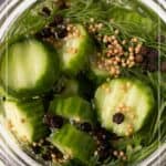 A jar of sliced cucumbers with dill, mustard seeds, and peppercorns in brine, labeled "Refrigerator Dill Pickles.