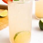 A glass of strawberry mojito mocktail garnished with a strawberry, lime slices, and mint leaves, on a white surface with a lime wedge nearby.