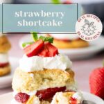 A plate with strawberry shortcake topped with whipped cream and fresh strawberries, with more shortcakes and strawberries in the background.