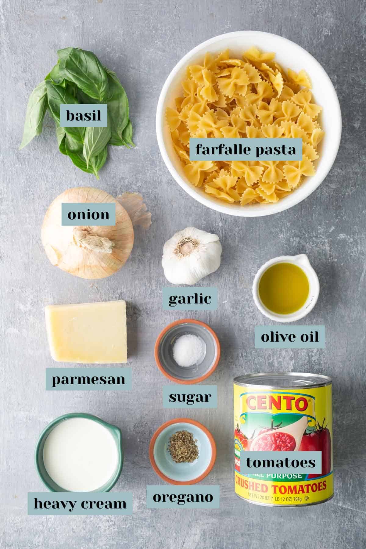 Top-down view of ingredients for pasta: farfalle pasta, basil, onion, garlic, olive oil, parmesan, sugar, oregano, heavy cream, and a can of crushed tomatoes.