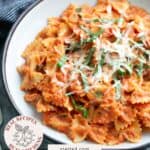 A bowl of bow-tie pasta with tomato basil sauce, topped with grated cheese and fresh basil, served on a gray plate.