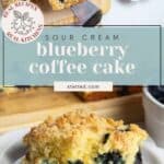A slice of blueberry coffee cake with crumb topping on a white plate, next to a serving spatula and more cake on a wooden board.