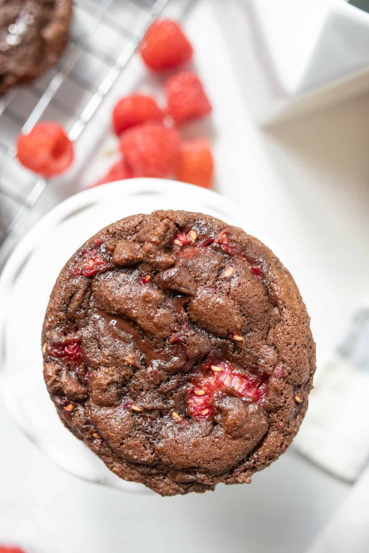 A chocolate raspberry cookie as seen from overhead with raspberries in the background.