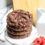 Four chocolate raspberry cookies stacked on a small white stand.