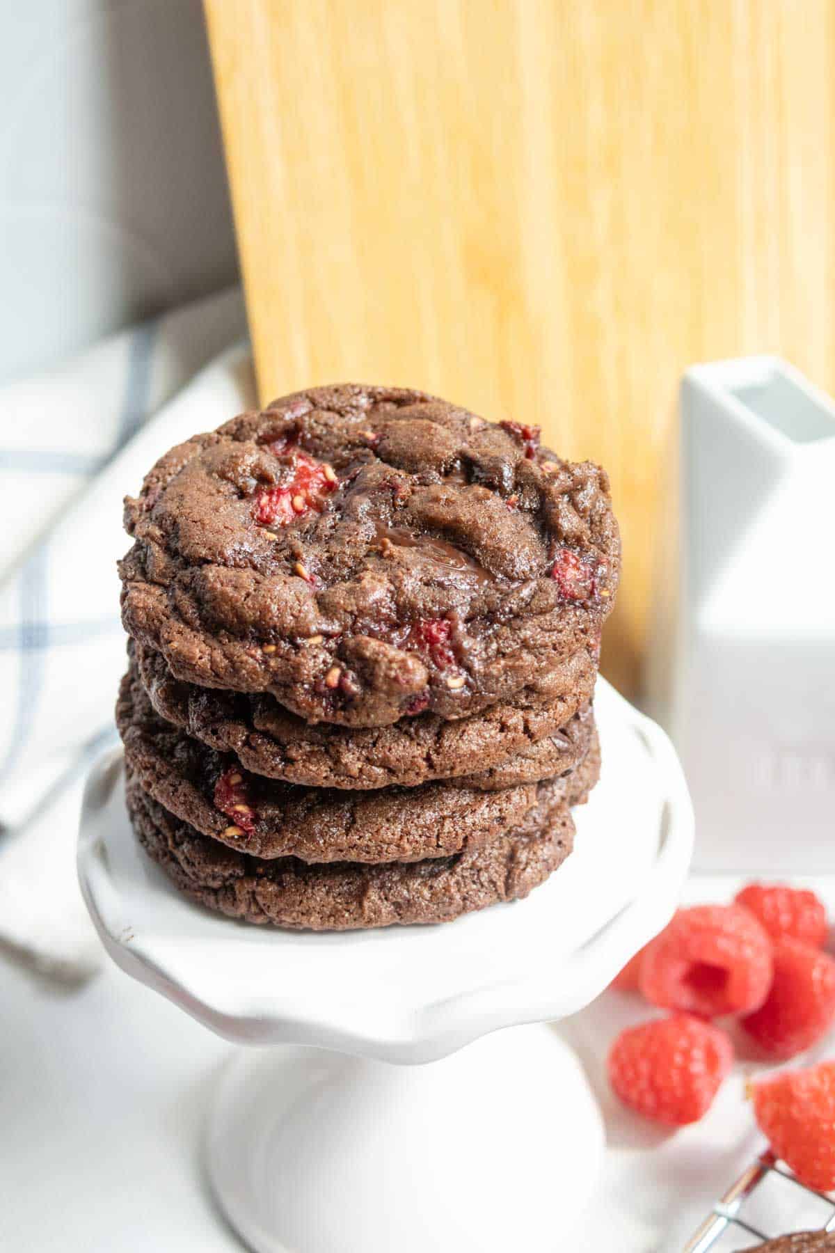 Four chocolate raspberry cookies stacked on a small white stand.