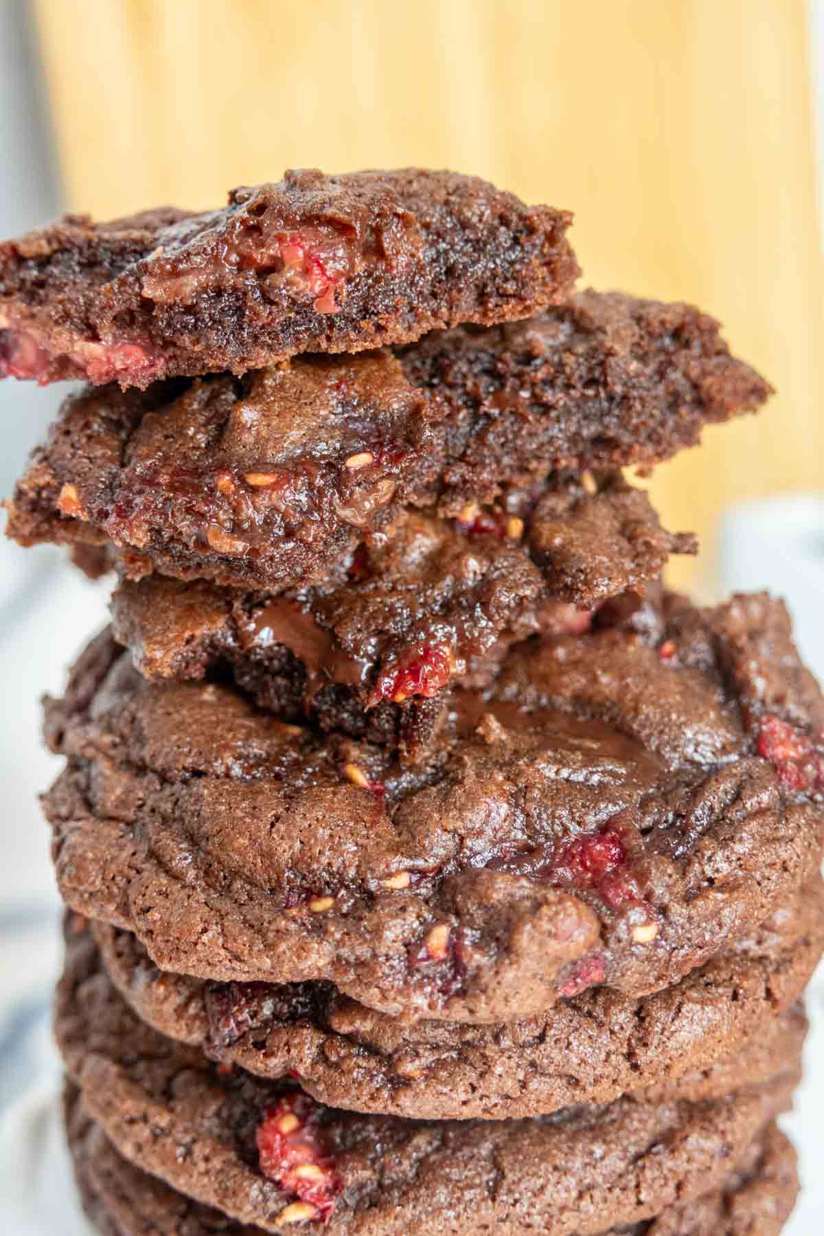 A stack of chocolate raspberry cookies with broken cookie pieces on top showing melty chocolate.