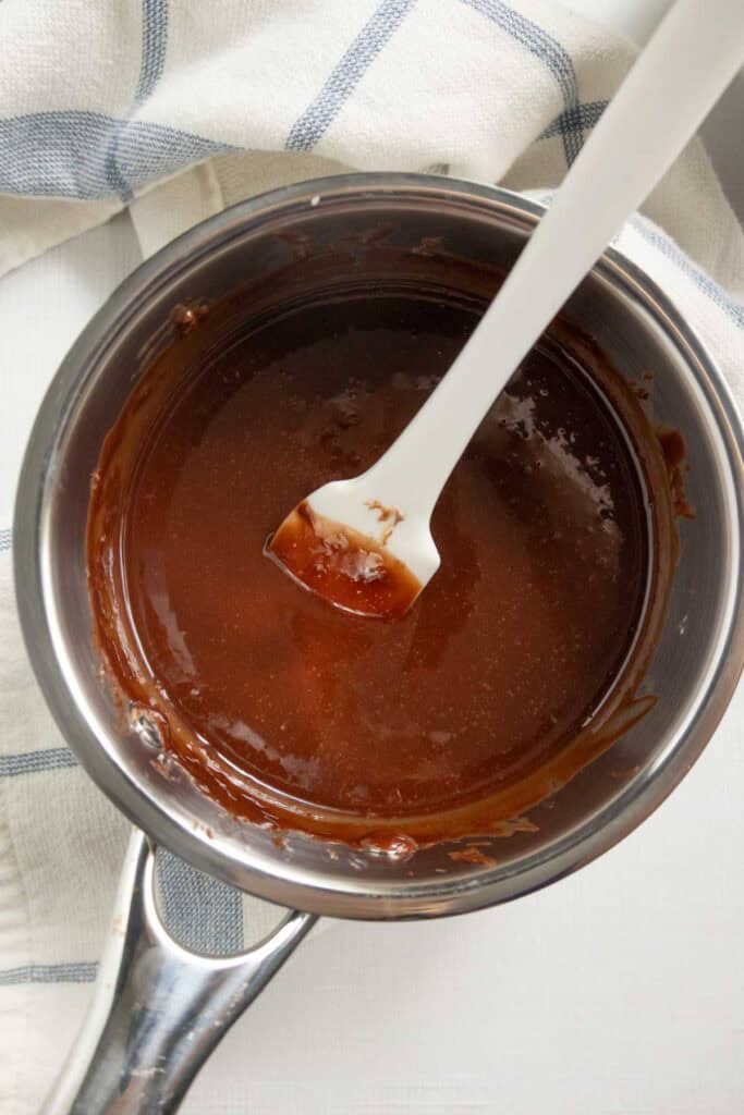 A saucepan filled with melted chocolate and a white spatula sticking out of it.