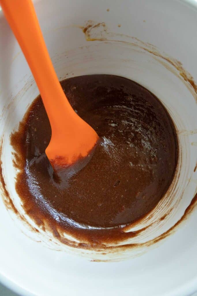 An orange spatula stirring chocolate batter in a white bowl.