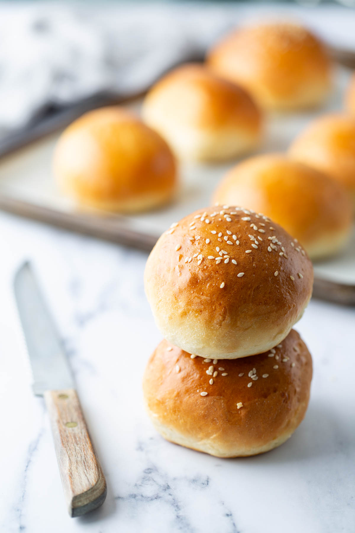 Two homemade burger buns stacked next to a knife.