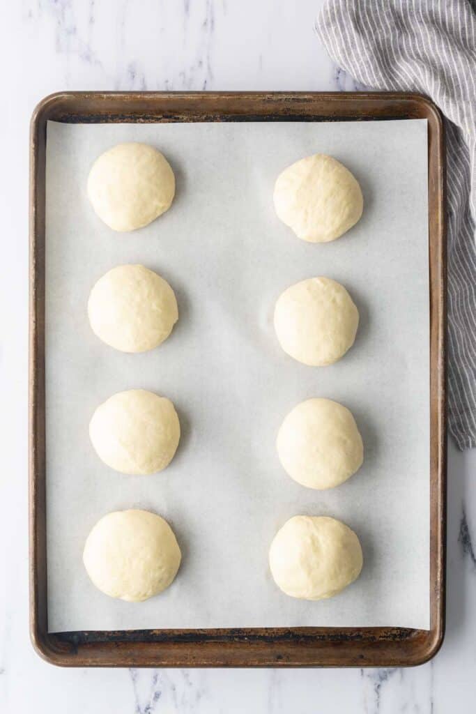Unbaked burger buns on a sheet pan.