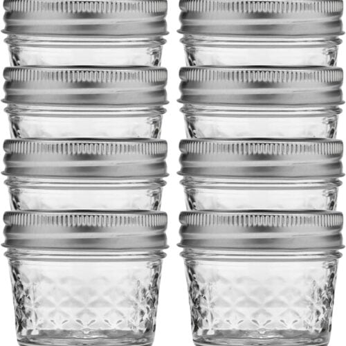 Eight small, empty glass jars with silver metal lids are arranged in two columns of four against a white background.