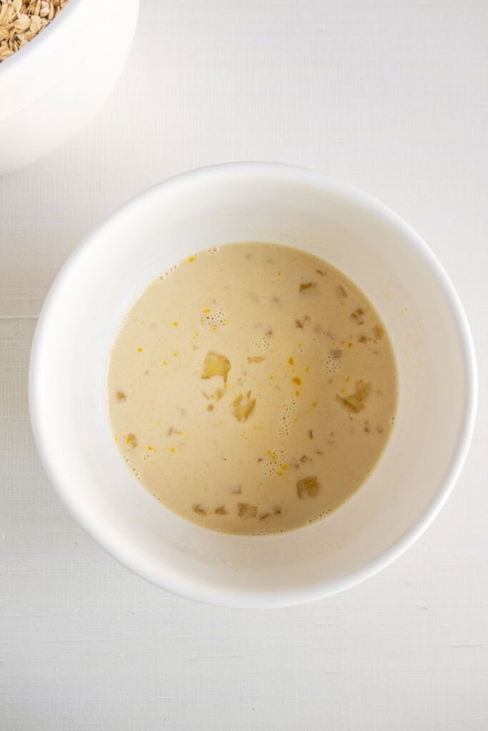White bowl containing a mixture of milk and egg on a light surface. Part of another bowl is visible at the top left corner.