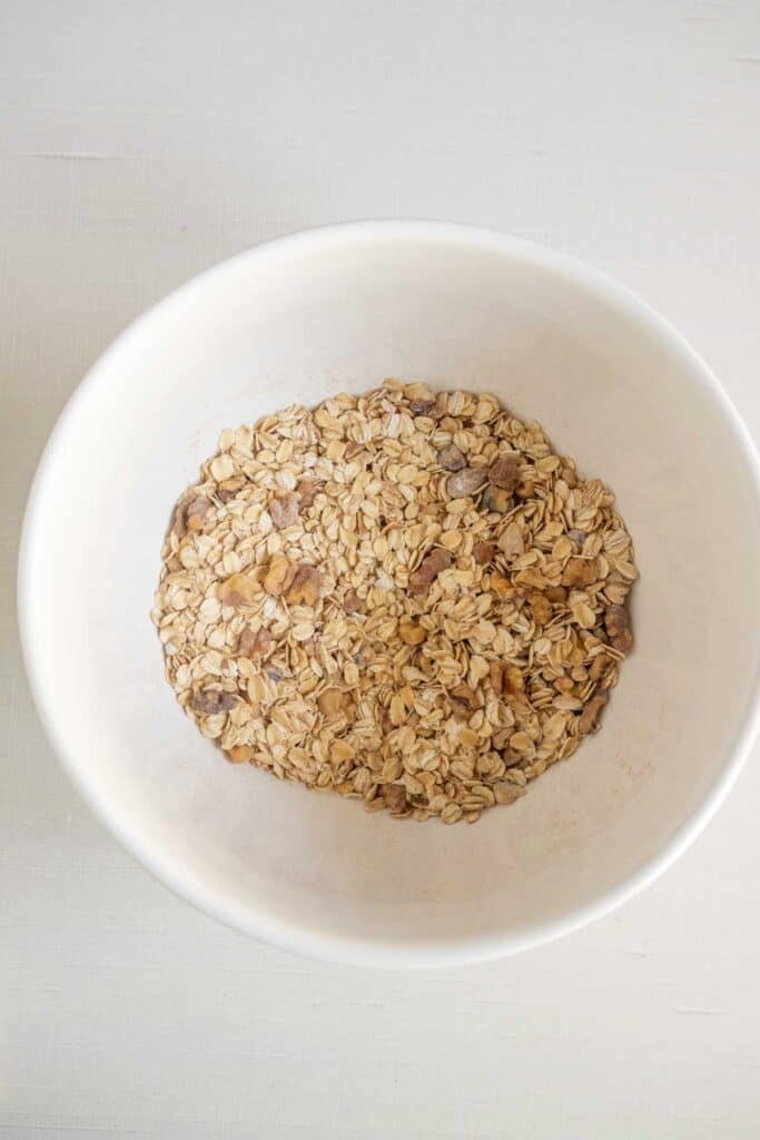 A white bowl filled with dry rolled oats sits on a light-colored surface.