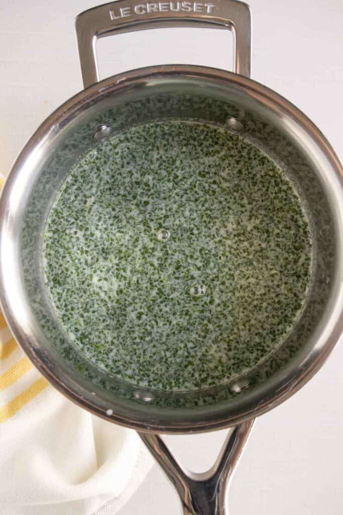 A stainless steel pot containing a creamy green mixture with finely chopped herbs, viewed from above.