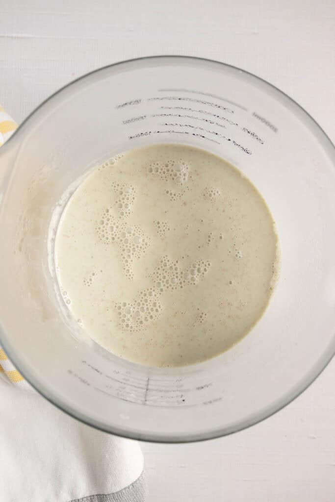 A glass measuring cup containing a frothy, beige liquid mixture viewed from above on a white surface.
