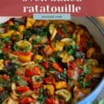 A blue casserole dish filled with oven-baked ratatouille made of sliced vegetables, garnished with chopped herbs, sits on a table next to a loaf of bread.