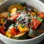 A bowl of baked ratatouille with chopped vegetables, tomato sauce, and grated cheese, garnished with fresh herbs. Text reads "baked ratatouille.