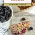 A slice of blackberry scone on a marble board with blackberries scattered around and a bowl of fresh blackberries nearby.