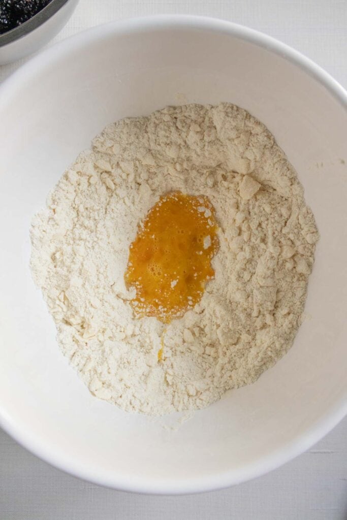 A white bowl containing flour with a well in the center holding a beaten egg.