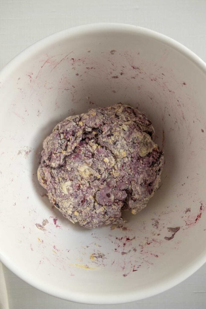 A ball of purple and beige dough sits in a white mixing bowl, with traces of dough and ingredients stuck to the sides.