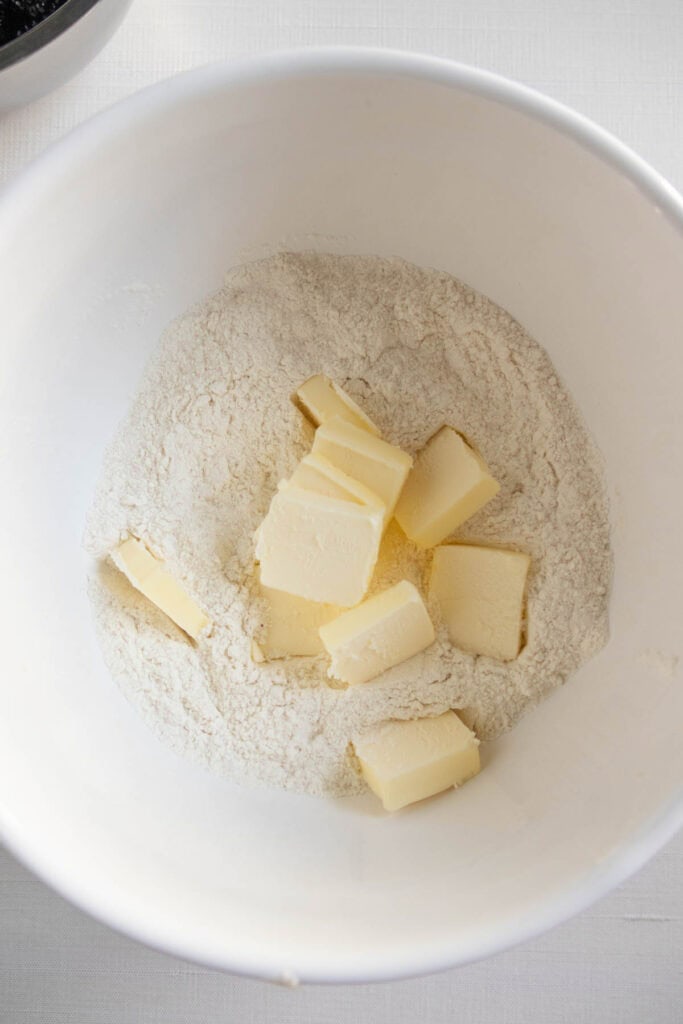Cubed butter sits on top of flour in a white mixing bowl, ready to be mixed together for a baking recipe.