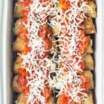 A baking dish filled with breaded eggplant rollatini topped with tomato sauce and shredded cheese, arranged in rows.